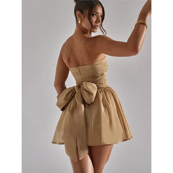 Vrouw in strapless gouden cocktailjurk met strik, elegante avondkleding, modieuze feestjurk, chique damesmode, stijlvolle outfit voor speciale gelegenheden.