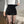 Vrouw in witte trui en zwarte corduroy shorts met hoge taille, toont verstelbare tailleband. Modieuze dameskleding, comfortabele pasvorm.