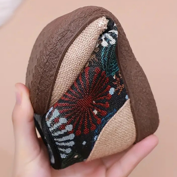 Hand houdt opvouwbare, bruine damesschoen met kleurrijk bloemenpatroon vast. Comfortabele, flexibele schoenen voor dagelijks gebruik.