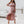 Vrouw in roze off-shoulder jurk met ruches, asymmetrische zoom en sandalen. Elegante zomermode, perfect voor feestelijke gelegenheden.