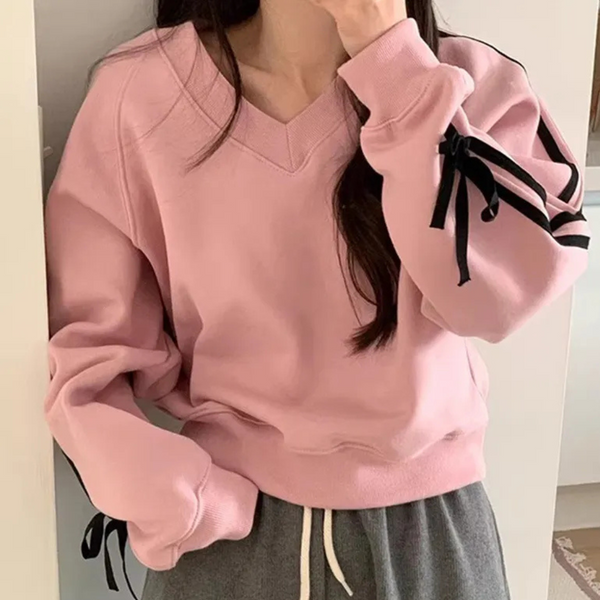 Vrouw in roze trui met zwarte strikdetails, casual mode, comfortabele kleding, trendy dameskleding, herfstoutfit, modieuze sweaterstijl.