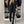 Vrouw in stijlvolle zwarte blazer met witte strepen, zwarte broek, en zwarte tas, poseert voor kledingkast. Modieuze dameskleding, chique outfit.