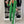 Vrouw in groene broekpak met witte strepen, zwarte top en handtas, voor kledingkast met schoenen. Modieuze dameskleding, trendy outfit.
