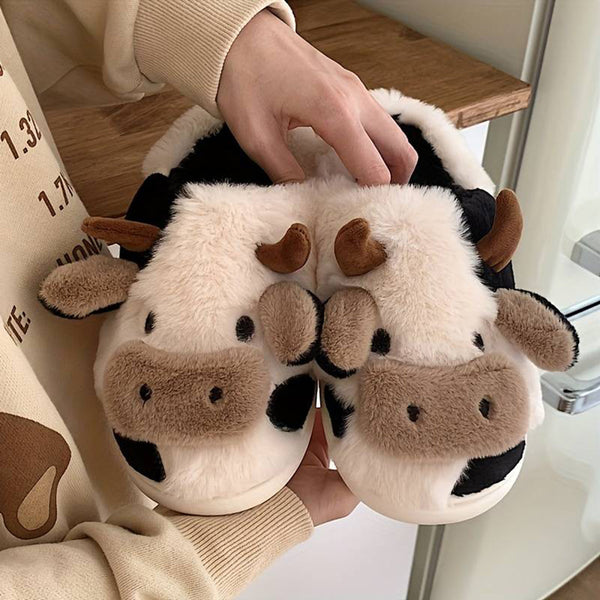 Pluche koe pantoffels met bruine hoorns en zwarte vlekken, vastgehouden door een persoon. Comfortabele, warme sloffen voor thuisgebruik.