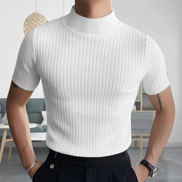 Man in witte gebreide trui met korte mouwen, staand in moderne woonkamer. Stijlvolle herenkleding, casual mode, minimalistisch interieur.