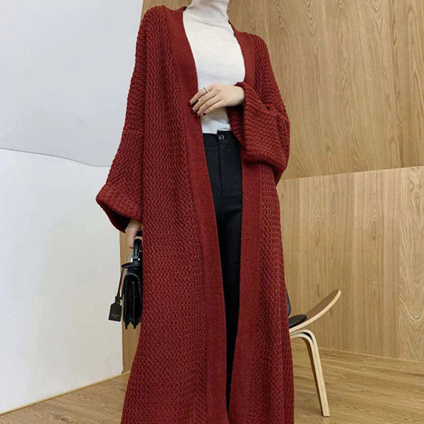 Rode gebreide damescardigan, lange mouwen, casual stijl, gedragen over witte coltrui en zwarte broek, moderne houten achtergrond.