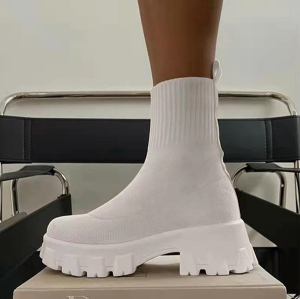 Witte enkellaars met dikke zool, gebreide schacht en modern design op zwarte stoel. Trendy damesmode, comfortabele en stijlvolle schoenen.