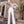 Vrouw in elegante witte jumpsuit met veren details, staand voor een stenen gebouw. Modieuze dameskleding, chique avondoutfit, trendy stijl.