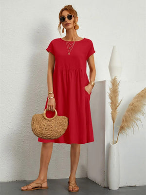 Vrouw in rode zomerjurk met zakken, vintage stijl, O-hals, draagt zonnebril en rieten tas, naast vaas met pampasgras.