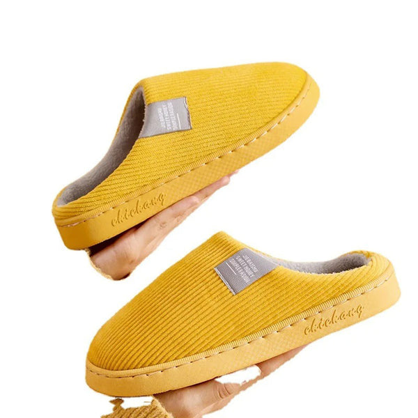 Gele pantoffels met grijze voering en label, comfortabele winterse huisschoenen, antislip zool, unisex design, perfect voor thuisgebruik.