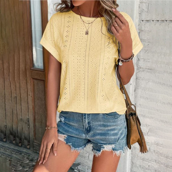 Vrouw in gele geperforeerde blouse en denim shorts, casual zomeroutfit, met bruine schoudertas, modieuze kledingstijl, buiten bij houten deur.