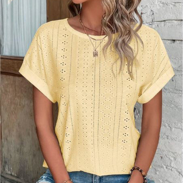 Vrouw in gele geperforeerde blouse, casual zomeroutfit, modieuze kleding, trendy damesmode, buiten bij muur, golvend haar, kettingaccessoire.