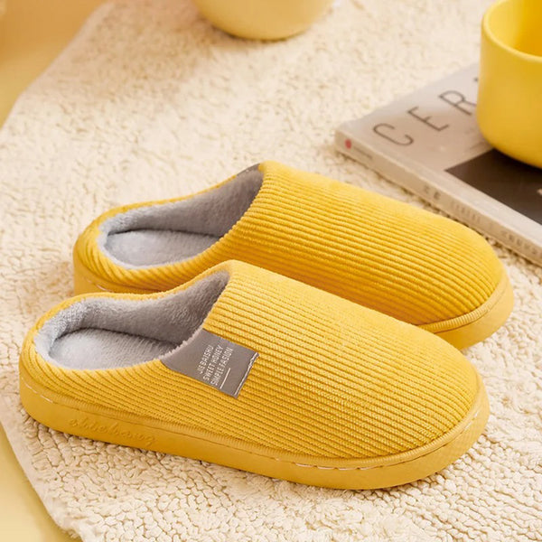 Gele pluchen pantoffels op beige tapijt, naast een tijdschrift en gele mok. Comfortabele huispantoffels, perfect voor binnengebruik.