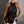 Vrouw in zwarte, mouwloze haltertop met glinsterende textuur, witte broek en bruine clutch. Stijlvolle zomermode, elegante avondlook.
