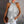 Vrouw in zilveren glittertop met halternek, witte broek en bruine clutch. Modieuze outfit voor avondje uit. Stijlvolle dameskleding.