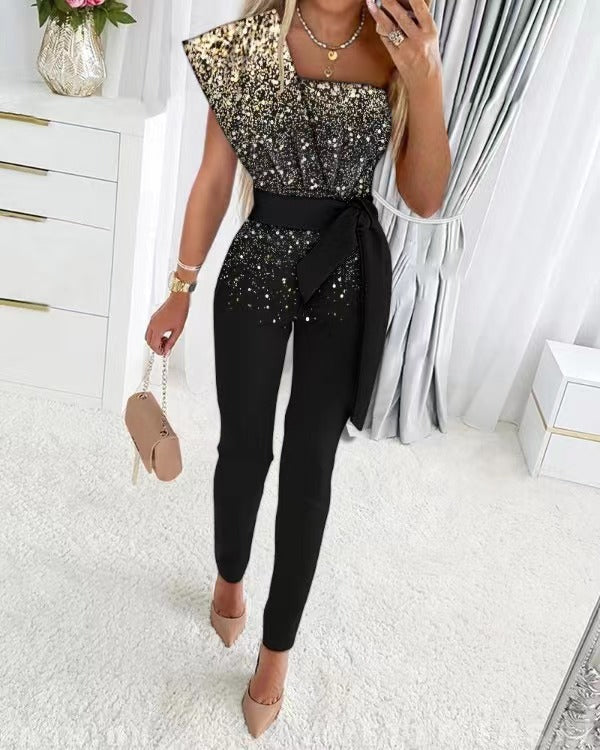 Vrouw in elegante zwart-gouden glitter jumpsuit met asymmetrische halslijn, zwarte riem, beige handtas en hakken, in moderne slaapkamer.