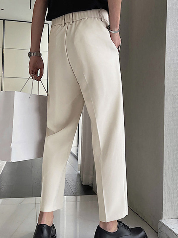 Man in moderne, crèmekleurige broek met zwarte schoenen, draagt witte papieren tas. Stijlvolle herenkleding, minimalistisch design, modeaccessoires.