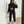Vrouw in zwarte joggingpak met crop top, witte sneakers en beige handtas, maakt selfie in spiegel. Modieuze sportkleding, casual stijl.