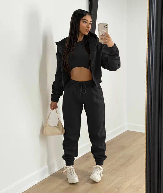 Vrouw in zwarte joggingpak met crop top, witte sneakers en beige handtas, maakt selfie in spiegel. Modieuze sportkleding, casual stijl.