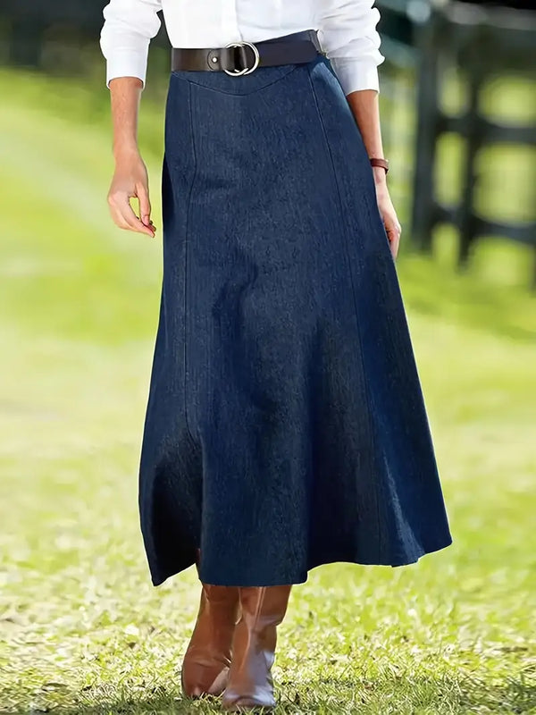 Vrouw in witte blouse en lange denim rok met riem, staand op grasveld. Stijlvolle herfstmode, casual outfit, dameskleding, bruine laarzen.
