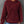 Vrouw in bordeauxrode gebreide hoodie met capuchon en buidelzak, casual stijl, gecombineerd met blauwe jeans, tegen grijze achtergrond.
