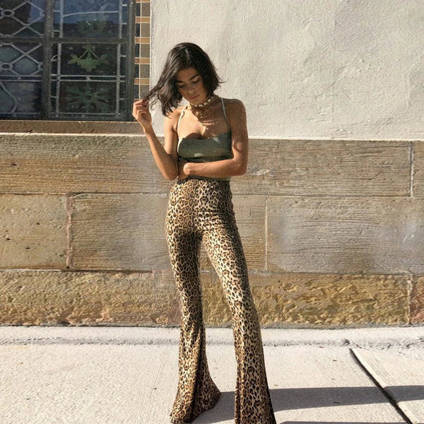 Jonge vrouw in luipaardprint broek en groene top poseert tegen stenen muur. Modetrend, stijlvolle outfit, casual chic look.