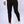 Man in zwarte slim-fit broek en witte sneakers, staand tegen een neutrale achtergrond. Modieuze herenmode, casual outfit, comfortabele stijl.