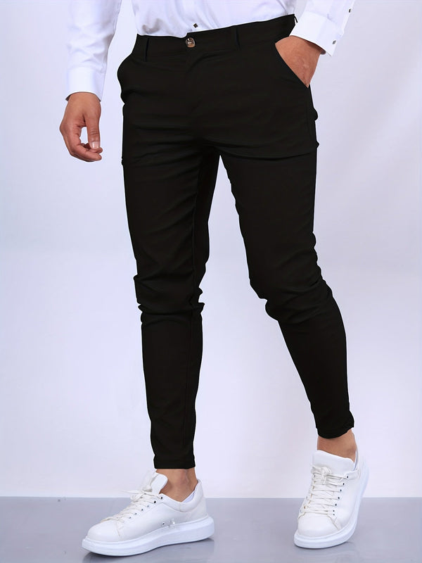 Man in zwarte slim-fit broek en witte sneakers, staand tegen een neutrale achtergrond. Modieuze herenmode, casual outfit, comfortabele stijl.