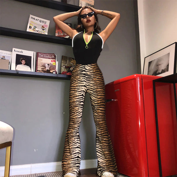 Vrouw in modieuze outfit met tijgerprint broek en zwarte top poseert voor rode koelkast. Trendy kleding, moderne stijl, interieurdecoratie.