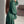Vrouw in groene lange jurk met pofmouwen, gefotografeerd van opzij in een moderne woonkamer. Trendy damesmode, elegante avondjurk.