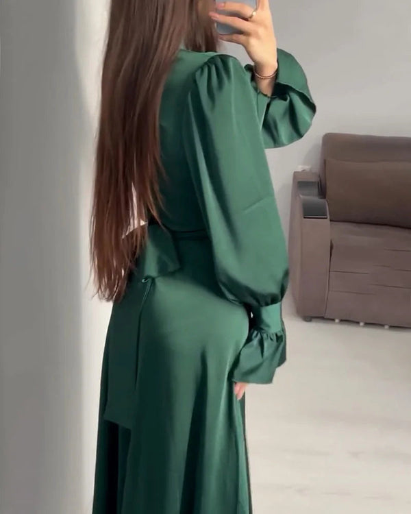 Vrouw in groene lange jurk met pofmouwen, gefotografeerd van opzij in een moderne woonkamer. Trendy damesmode, elegante avondjurk.