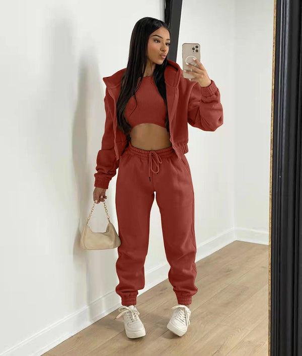 Vrouw in terracotta trainingspak met crop top en hoodie, poseert voor spiegel met beige handtas en smartphone, modieuze sportkleding.