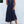 Vrouw in elegante, donkerblauwe zomerjurk met knopen, staand tegen witte muur. Perfecte outfit voor casual en chique zomermode.