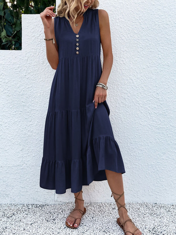 Vrouw in elegante, donkerblauwe zomerjurk met knopen, staand tegen witte muur. Perfecte outfit voor casual en chique zomermode.