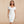 Vrouw in elegante witte off-shoulder bodycon jurk, V-hals, knie-lengte, geschikt voor zomerfeest of club, met clutch en oorbellen.