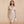 Vrouw in elegante beige off-shoulder bodycon jurk, V-hals, knie-lengte, met clutch. Perfect voor zomerfeest of club. Trendy en stijlvol.