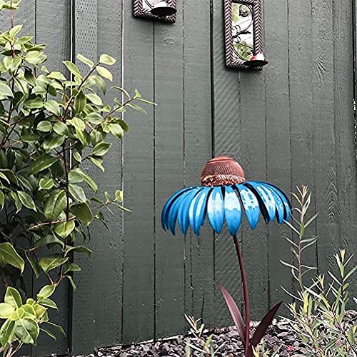 Blauwe metalen vogelvoeder in bloemvorm in tuin, omgeven door groene planten en houten schutting. Perfect voor tuindecoratie en vogelvoeding.