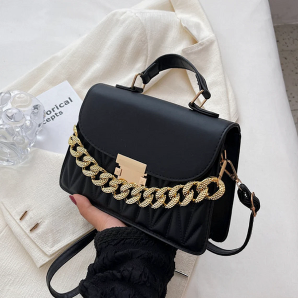 Zwarte leren handtas met gouden ketting, elegant design, damesmodeaccessoire, trendy schoudertas op witte achtergrond, stijlvolle uitstraling.