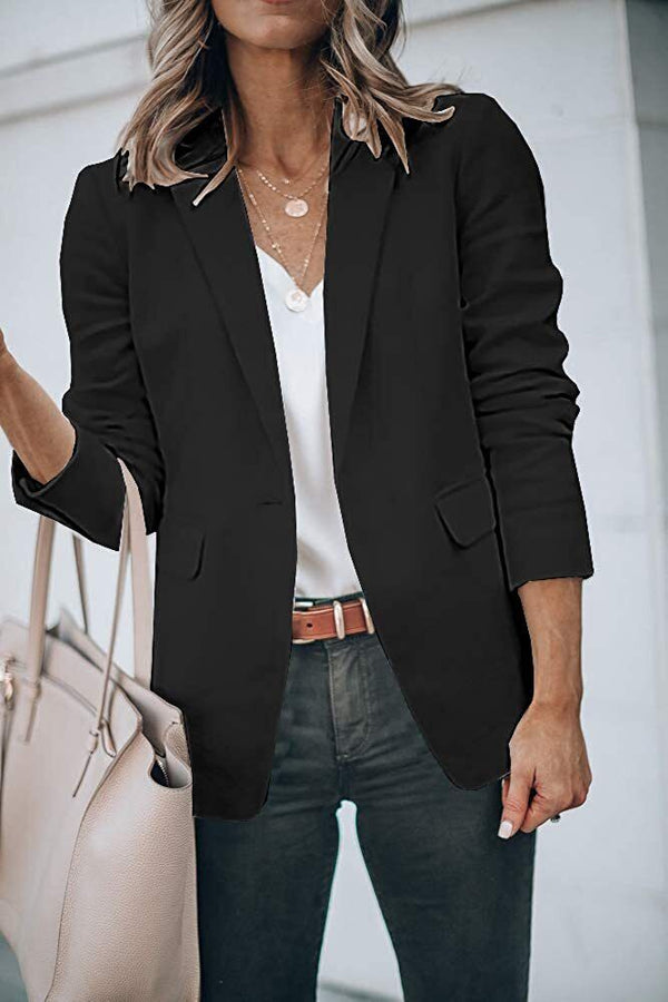 Vrouw in zwarte blazer met witte blouse en spijkerbroek, draagt een beige handtas. Stijlvolle zakelijke outfit voor damesmode.