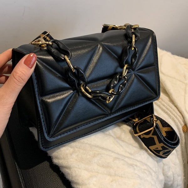 Zwarte leren handtas met gouden ketting en geometrisch patroon, vastgehouden door een hand. Luxe damesaccessoire, modieuze schoudertas.
