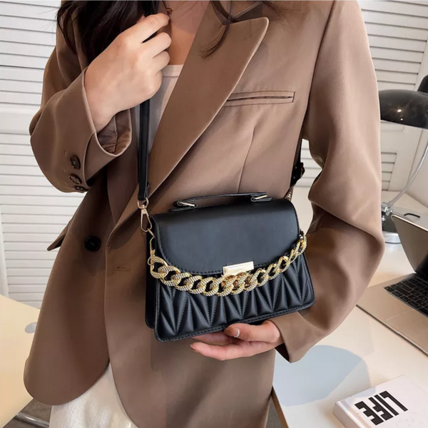 Vrouw met bruine blazer houdt stijlvolle zwarte handtas met gouden ketting vast. Modieuze damesaccessoire, elegant design, trendy look.