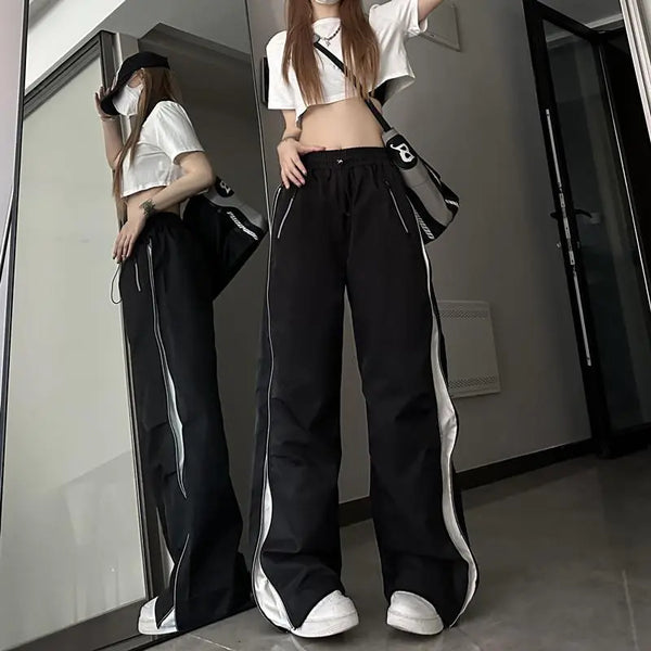 Vrouw in trendy zwarte wijde broek met witte strepen, crop top en pet, poseert voor spiegel. Streetwear mode, casual outfit, urban stijl.