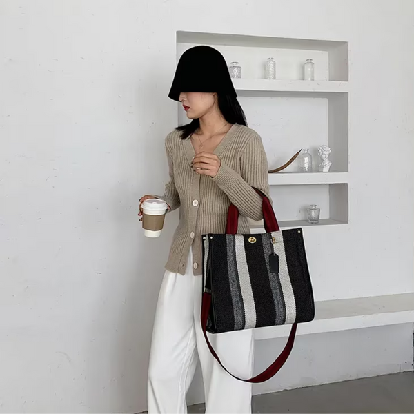 Vrouw met zwarte hoed en beige vest draagt een gestreepte zwarte tas en houdt een koffiebeker vast. Stijlvolle mode, casual outfit, trendy accessoires.