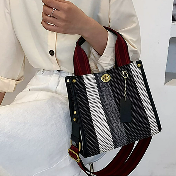 Zwart-witte gestreepte handtas met rode handvatten, gedragen door persoon in witte blouse. Modieuze damesaccessoire, trendy design.