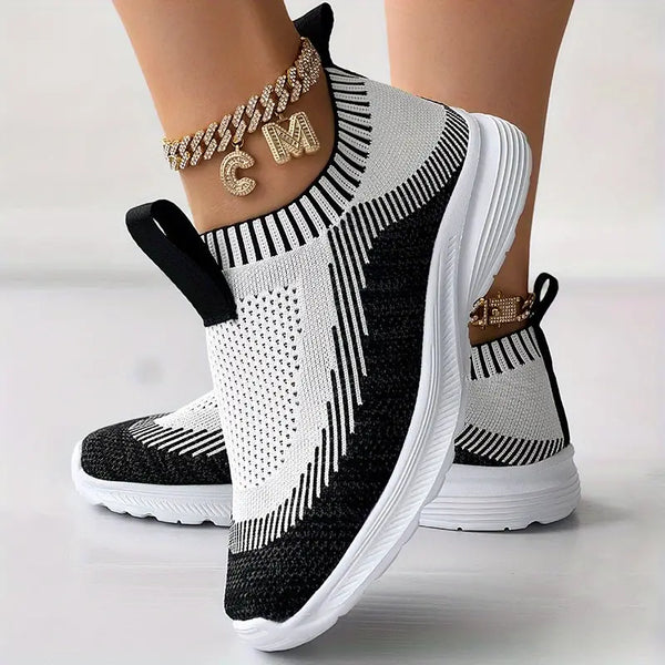 Zwart-witte gebreide sneakers met dikke zool en gouden enkelband met initialen. Moderne damesmode, comfortabele sportschoenen.