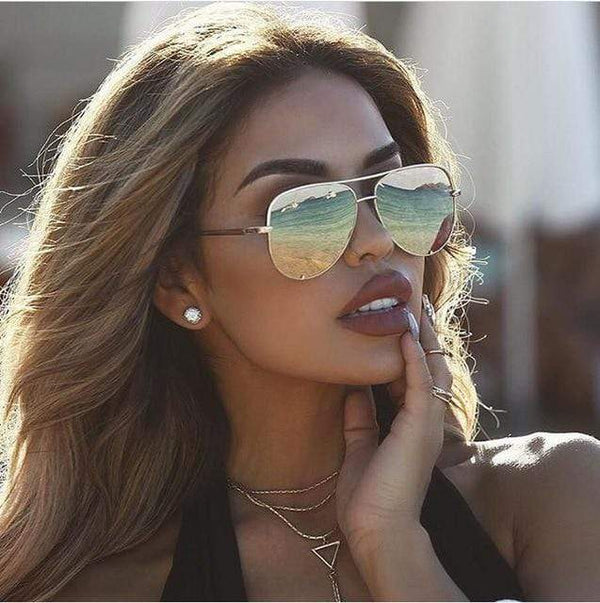 Vrouw met designer aviator zonnebril, goudkleurig montuur, weerspiegeling van strand en zee, stijlvolle zomermodeaccessoire.