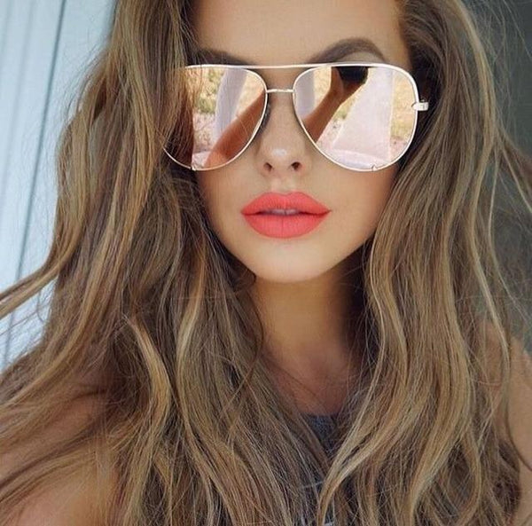 Vrouw met lange golvende haren draagt roze aviator zonnebril en feloranje lippenstift. Modieuze dameszonnebril, trendy accessoire.