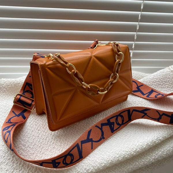 Bruine leren handtas met gouden ketting en verstelbare schouderriem, geometrisch ontwerp, op witte achtergrond. Luxe damesaccessoire.