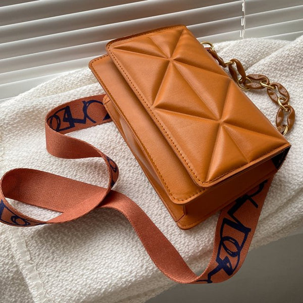 Bruine leren schoudertas met geometrisch patroon en verstelbare riem, liggend op witte stof. Stijlvolle damesaccessoire, trendy design.
