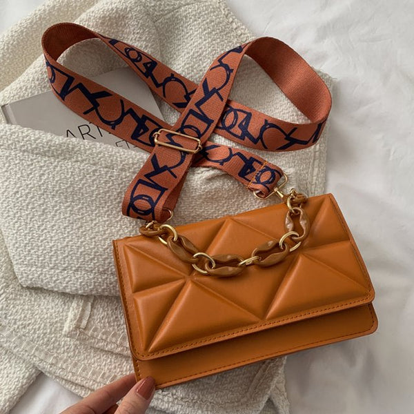 Bruine leren handtas met gouden ketting en verstelbare schouderriem, stijlvolle damesmodeaccessoire op witte stoffen achtergrond.